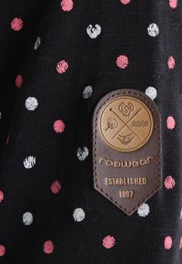 Tela negra con lunares multicolores (rosa, blanco, gris). Presenta un parche de cuero marrón con un logo en relieve y el texto "radwear ESTABLECIDO 1997."
