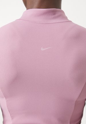 Zbliżenie górnej części pleców osoby ubraną w różowy top Nike z małym, jasnoróżowym logo Nike swoosh umieszczonym na środku pod kołnierzem.