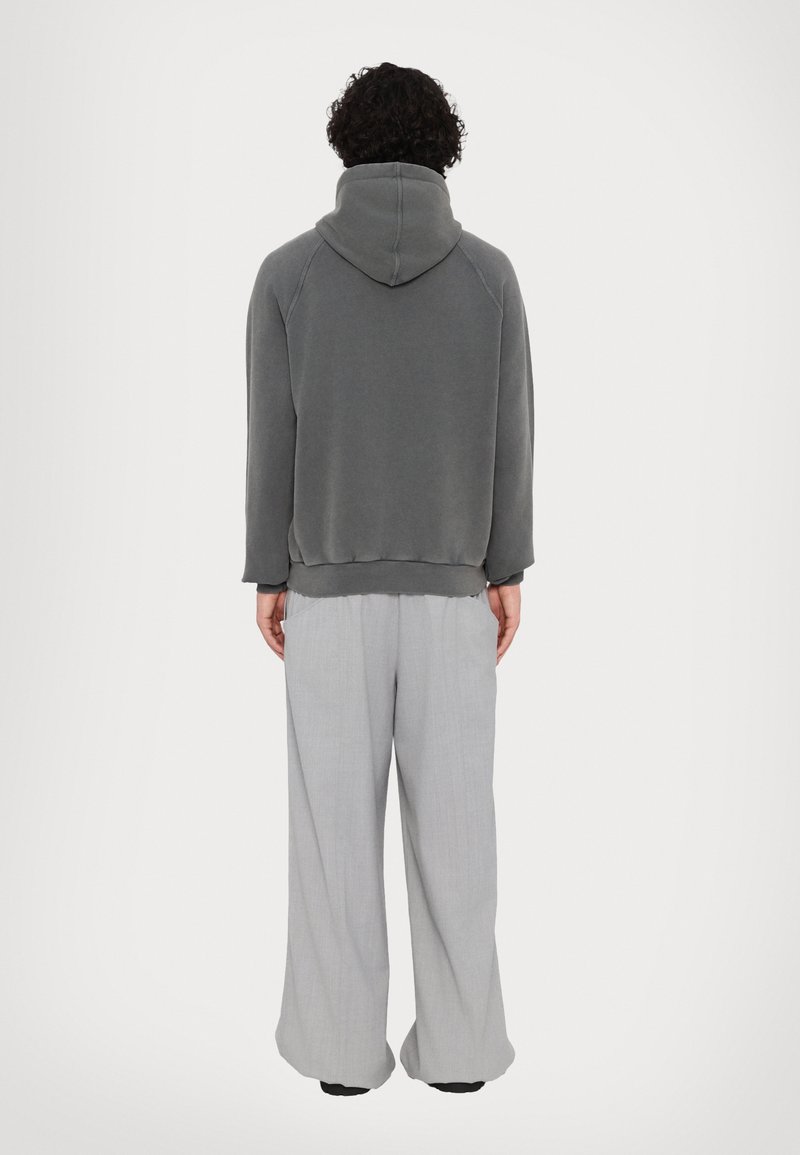Haut à capuche gris avec un col haut, coupe décontractée et poignets côtelés. Porté sur un pantalon large gris clair. Texture de tissu lisse, design simple.