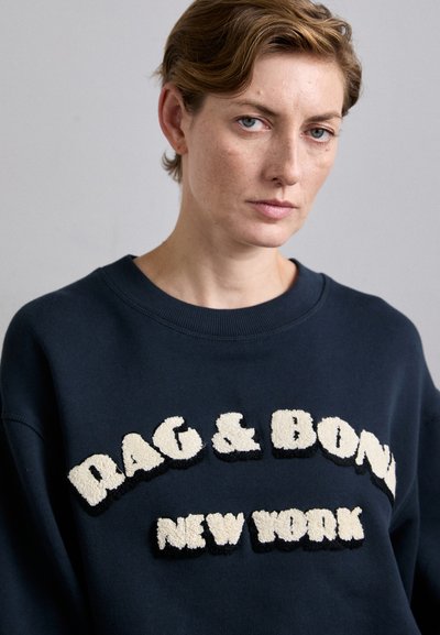 Granatowy polar z teksturowanym kremowym i czarnym haftowanym napisem "RAG & BONE NEW YORK" z przodu. Okrągły dekolt, miękka tkanina.
