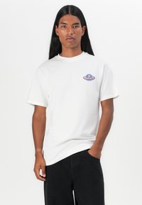 White cotton t-shirt with short sleeves and a round neckline. Features a colorful alien spaceship graphic on the left chest.