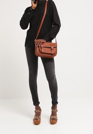 Borsa a tracolla in pelle marrone con doppi fibbie, abbinata a top in pizzo nero, jeans skinny grigi e sandali platform con stampa animalier.