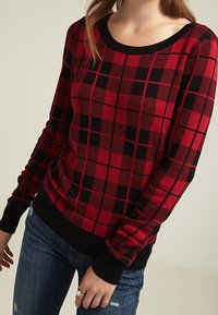 Röd och svart rutigt tröja med långa ärmar, ribbad halsringning och nederkant, tillverkad av stickat tyg, med en boxig passform och texturmönster.