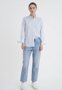 Light blue button-up shirt with a collar, paired with faded blue straight-leg jeans and white sneakers. Minimal design, no visible patterns.