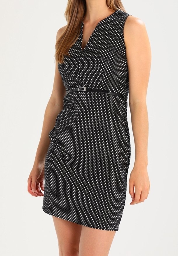 Robe sans manches noire avec des pois blancs, coupe ajustée, taille ceinturée discrète et tissu texturé, avec un décolleté en V.