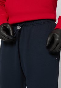 Marineblå sweatpants med elastisk midje og snøring, med et lite logomerke og glatt tekstur. Kombinert med en rød hettegenser.