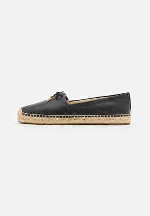 Zwarte leren espadrille met platte zool, met jute touw details op de zool en een kleine zwarte strik met gouden accenten aan de voorkant.