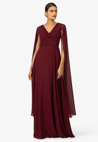 Abito da sera bordeaux in tessuto fluido caratterizzato da scollatura a V, corpino plissettato e maniche a cappotto trasparenti, creando una silhouette elegante.
