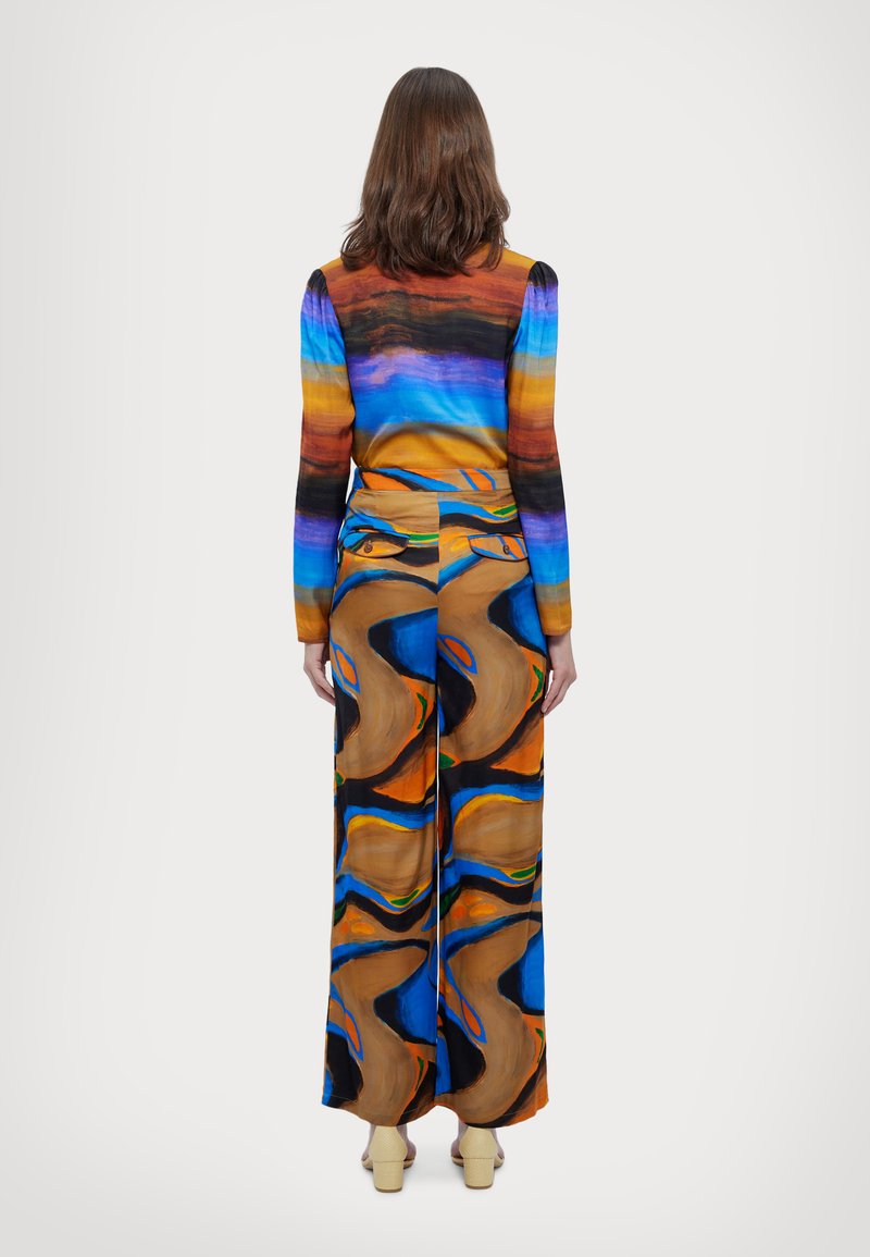 Wielokolorowa bluzka z długim rękawem w niebieskie, pomarańczowe i brązowe paski zestawiona z szerokimi spodniami w abstrakcyjne wielokolorowe wzory.