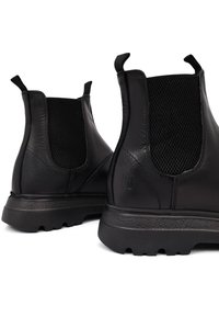Botas negras de cuero hasta el tobillo con acentos de malla, tiradores y suelas texturizadas. Presenta un acabado suave y un diseño de punta redondeada.