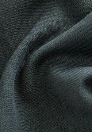 Tmavě zelená texturovaná látka s hladkým pleteným vzorem. Materiál se zdá být měkký a lehce elastický, ukazuje záhyby a sklady.