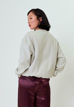 Hellgraues oversized Sweatshirt mit gerippten Bündchen, kombiniert mit glänzenden, tief burgunderfarbenen Hosen. Glatte Textur und lässige Passform.