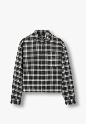 Juoda ir pilka languota ilgomis rankovėmis mygtukais užsegama marškinėliai su apykakle ir krūtinės kišene, išsiuvinėta ranka rašyto stiliaus raide „B“, baltame fone.