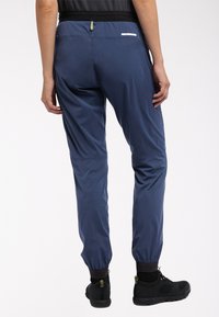 Marineblauwe lichtgewicht broek met een taps toelopende pasvorm, elastische boorden en een zwarte tailleband. Heeft een achterzak met een rits en reflecterende details.