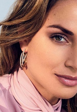 Guldøreringe med snoede sølvdetaljer prydet med små klare sten. Glat hud med en subtil, naturlig læbefarve og bløde scarf-detaljer.