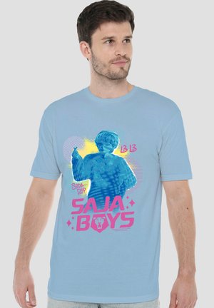 Man wearing a light blue t-shirt with a colorful graphic of a child and text "SAJA BOYS" in pink on the front.
