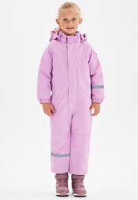 Roze winteroverall met een capuchon, elastische manchetten, reflecterende strepen en een soepele textuur. Gecombineerd met bruine en roze sneeuwlaarzen.