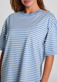 Light blue striped T-shirt with short sleeves, round neckline, and a small chest pocket. Fabric appears soft with a smooth texture.