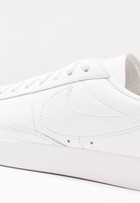 White leather sneakers with a textured Swoosh logo, round laces, and a flat rubber sole. Stitching detail adds definition to the design.
