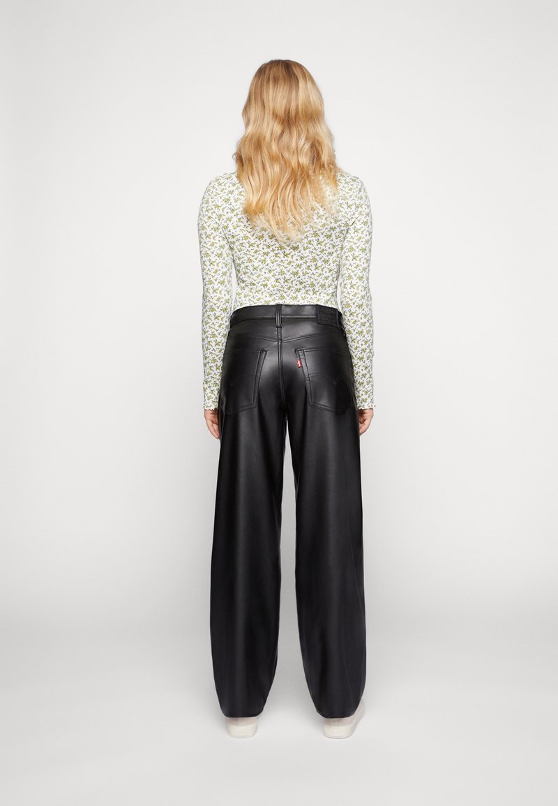 Zwarte leren brede broek met een gladde textuur, voorzien van twee achterzakken en een zichtbaar merklabel. Model draagt een bloemenprint lange mouwen top.