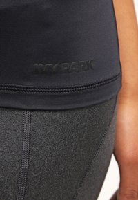 Top corto sportivo nero in tessuto testurizzato e design senza cuciture, con logo "IVY PARK" in finitura opaca lungo l'orlo.