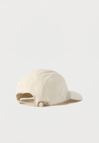 Μπεζ καπέλο με καμπυλωτό γείσο, διάτρητα πάνελ για αερισμό και ρυθμιζόμενο λουρί στο πίσω μέρος. Υφασμάτινη επιφάνεια με υφή και ομαλή τελειότητα.