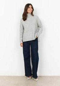 Light gray turtleneck sweater with a relaxed fit and side slits, paired with dark blue wide-leg jeans and embellished pointed-toe heels.