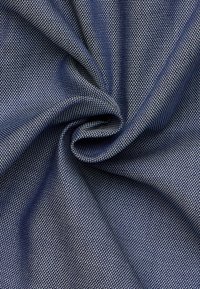 Marineblauwe stof met een gestructureerde weving, voorzien van een klein, uniform wit patroon. Zacht, valt soepel met een lichte glans.