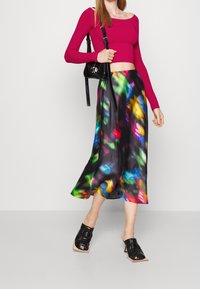 Top corto de canalé magenta ajustado combinado con una falda midi de satén negra que presenta un vibrante patrón abstracto de colores, y unas sandalias de tacón abiertas negras.