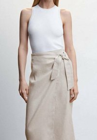 Top sans manches blanc à côtes associé à une jupe en lin beige à enveloppe, avec un détail de nouage sur le côté et une texture lisse.