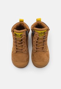 Stivali alla caviglia in suede marrone con suola in gomma, dotati di etichetta gialla sulla linguetta, lacci e cerniere laterali per una facile calzata.