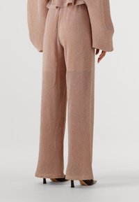 Broek in ribbelstructuur, lichtroze stof met een lichte glans. Ontwerp met wijde pijpen en een relaxte pasvorm, de zoom eindigt bij de enkel.