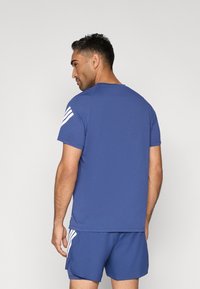 Camiseta deportiva azul de manga corta, hecha de un material suave. Presenta detalles de tres rayas blancas en el hombro izquierdo.