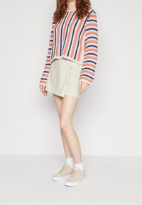 Pull rayé corail, marine et crème ; mini-jupe crème ; baskets beige à semelles blanches ; tricot texturé ; coupe décontractée ; manches longues.