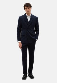 Traje azul marino de rayas diplomáticas, de corte cruzado y con solapas muesca, combinado con una camisa blanca y zapatos de cuero negros. Ajuste entallado y diseño estructurado.