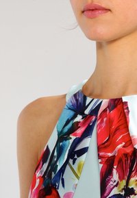 Floral-patterned halter neck top featuring vibrant colors including red, blue, and green, with soft fabric and a fluid, draped design.