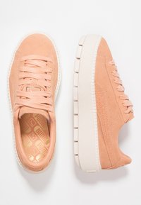 Meruňkové semišové tenisky s texturovaným povrchem, plochými tkaničkami, polstrovaným límcem a robustní bílou gumovou podrážkou s drážkami.