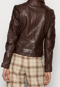 Hnědá kožená bunda s prošívanými akcenty na ramenech, obepínající střih a texturovaný povrch, spárovaná s kostkovanými kalhotami.