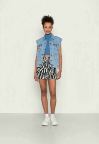 Jaqueta de ganga sem mangas, top cropped com efeito plissado azul e calções à zebra em preto e branco, combinados com ténis brancos e meias de tornozelo.