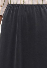 Μαύρη φούστα μέχρι το γόνατο με σούρα στη μέση και λεία υφή. Συνδυάζεται με ένα ανοιχτό ροζ ριγέ πουκάμισο με κουμπιά.