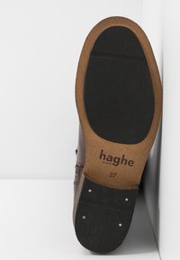 Semelle de chaussure marron avec une partie inférieure en caoutchouc noir texturé et un bord en bois. Marques comprenant "haghe by HUE" et la taille 37.