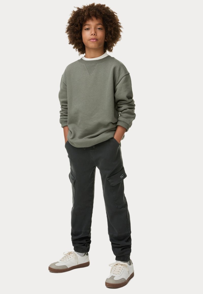 Donkergroene sweatshirt met geribbelde halslijn, zwarte cargobroek met zijzakken en witte sneakers met beige accenten. Casual pasvorm en stijl.