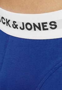 Boxer shorts de algodón azul con una cinturilla elástica blanca que presenta "BLACK & JONES" en letras negras. Textura suave, corte ajustado.