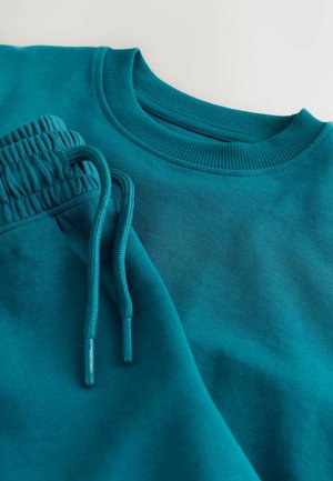 Hanorac turcoaz și pantaloni de trening asortați, cu manșete și talie cu nervuri, șireturi și textură netedă a țesăturii.