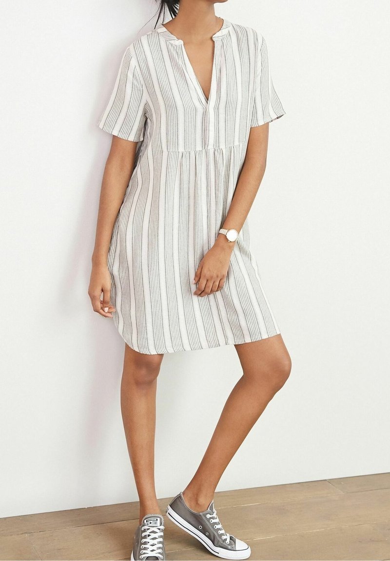 Robe à manches courtes rayée en blanc et gris, avec une légère forme évasée et un col en V, associée à des baskets grises.