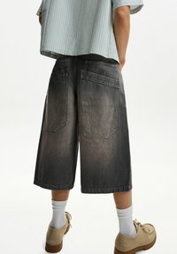 Denimshorts i falmet sort, knælang, med to baglommer. Båret med hvide ribbede strømper og beige sko. Fladstrikket lyseblå top.