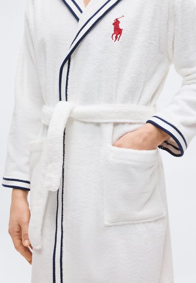 Λευκή ρόμπα από πετσέτα με μπλε ναυτικό πέπλο, δεμένη ζώνη, εμπρόσθιες τσέπες και κόκκινο κεντημένο λογότυπο παίκτη πόλο στο στήθος.