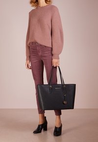 Sort læder tote taske med en struktureret design, guldfarvet hardware og en nøglering. Båret sammen med en ribbet lyserød sweater og burgunder bukser.