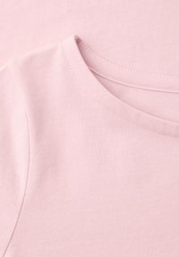 T-shirt en coton à manches courtes de couleur rose pâle, montrant les détails de la couture de l'encolure et de la couture d'épaule sur un fond uni.