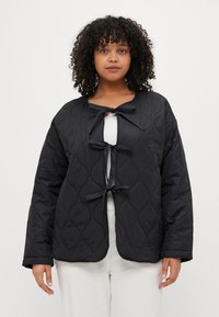 Zwarte gevoerde jas met een ronde kraag, drie lus-knoopsluitingen aan de voorkant en lange mouwen. Soepele stof met een lichte glans.